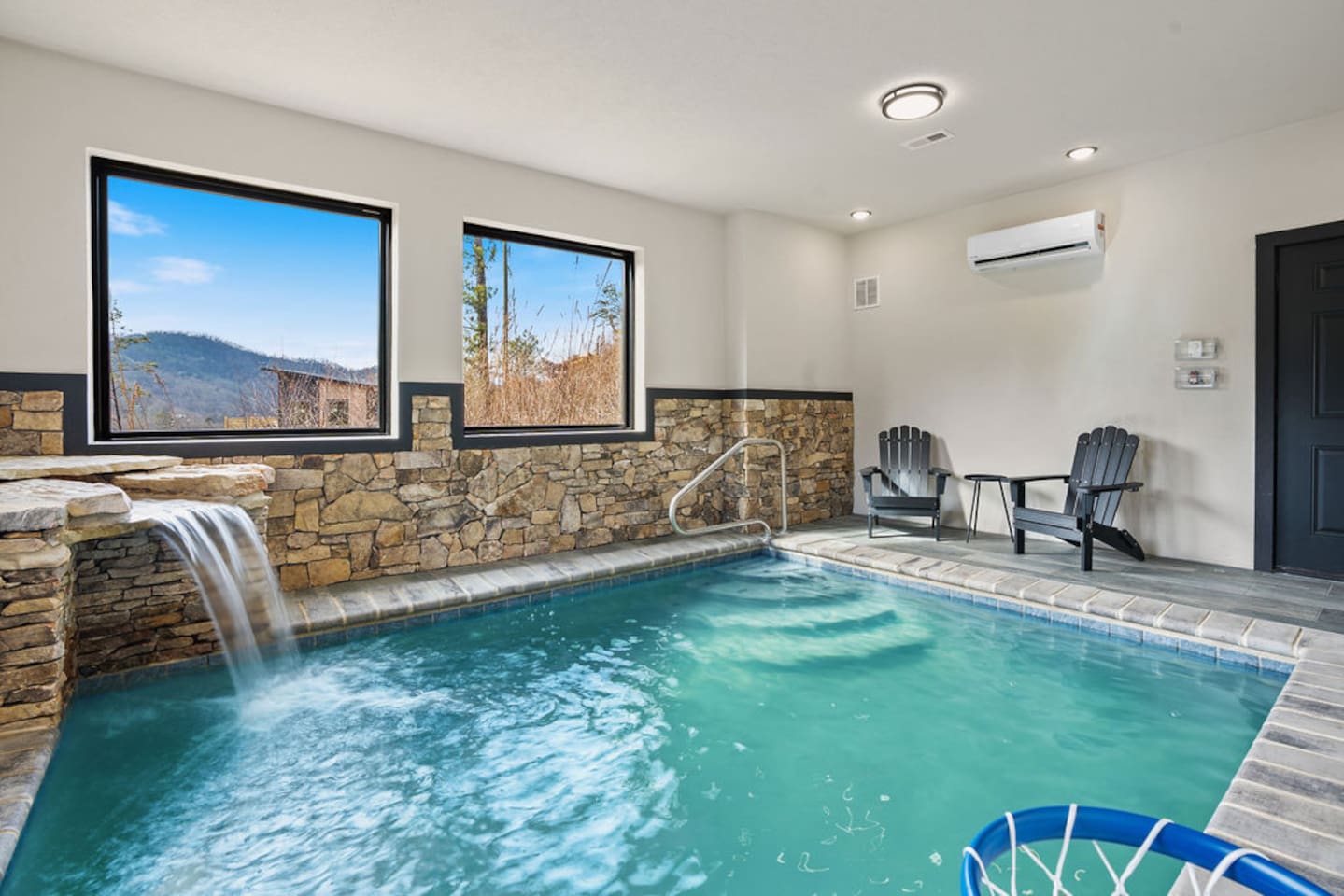 Private indoor pool with stone walls, waterfall feature, and mountain views through the windows